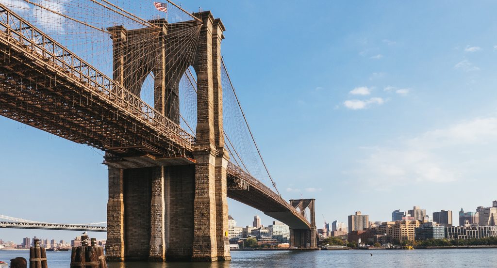 Iconic stone towers and suspension cables of the Brooklyn Bridge under a clear blue sky.