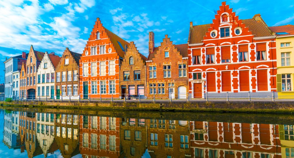 Vibrant stepped-gable houses lining a tranquil Brugge canal on a clear blue day.