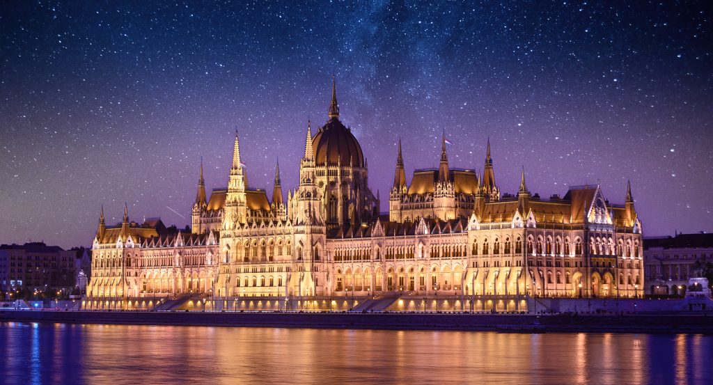 Glowing neo-Gothic architecture of Budapest’s Parliament lit up along the riverfront with a sparkling Milky Way above.
