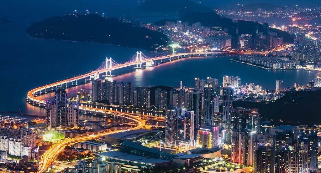 Nighttime view of Busan with bright city lights and illuminated bridge