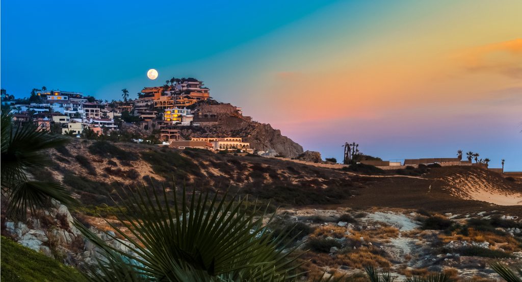 Dramatic sea cliffs and luxury villas in Cabo San Lucas, Mexico, with clear turquoise waters and palm-lined terraces.