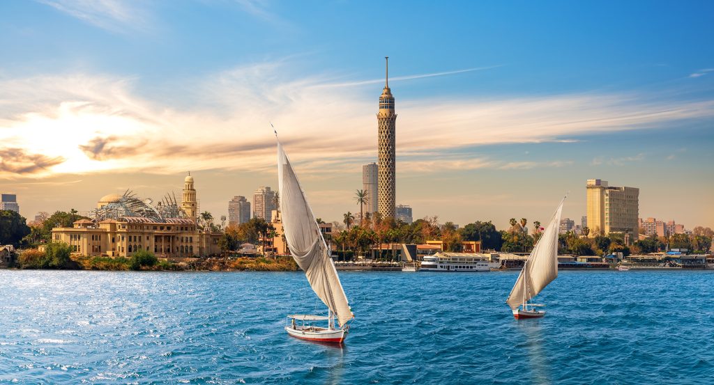 Traditional boats on the Nile with the iconic latticework Cairo Tower rising above the modern cityscape.