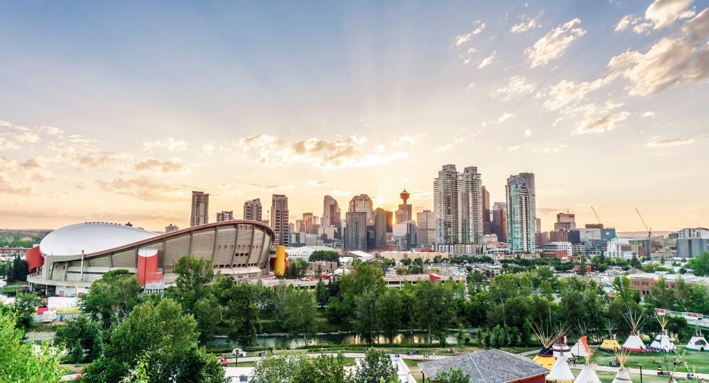 Skyline of Calgary at daybreak with rays of sun streaming through clouds behind modern towers.