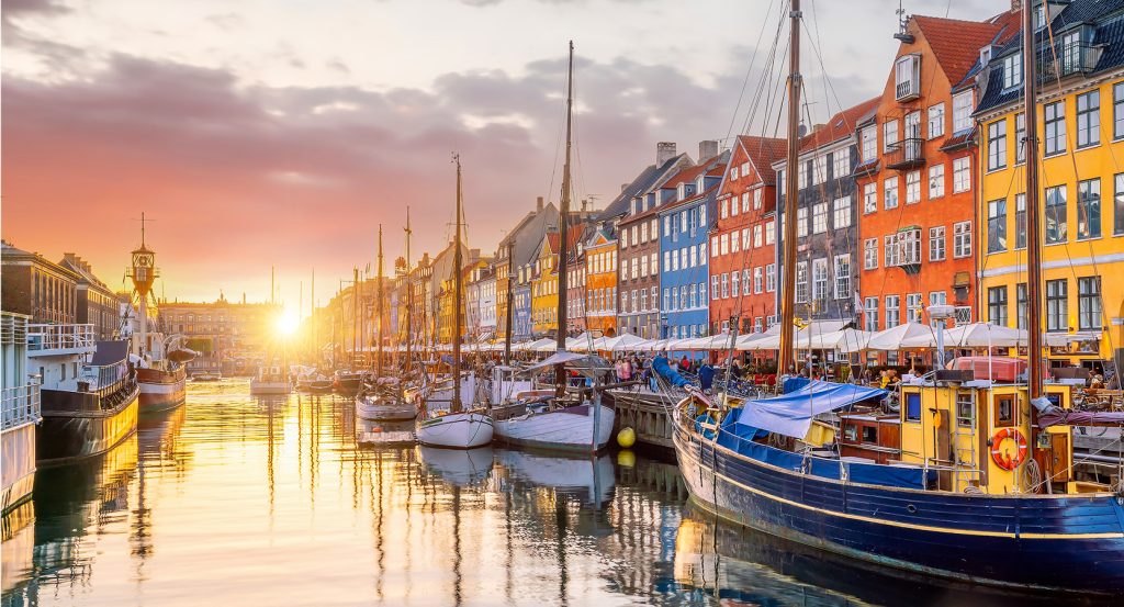 Golden-hour reflections shimmer along Copenhagen’s iconic waterfront, with cozy cafés and vibrant facades.