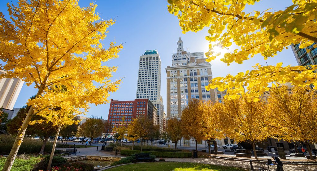 Sunlit fall scene in Tulsa, Oklahoma, with vibrant yellow leaves and vintage towers set against a clear blue sky.