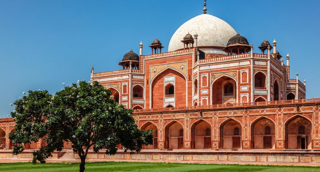 Front view of Humayun’s Tomb in Delhi, India, showcasing red sandstone arches, white marble dome, and lush garden in foreground.