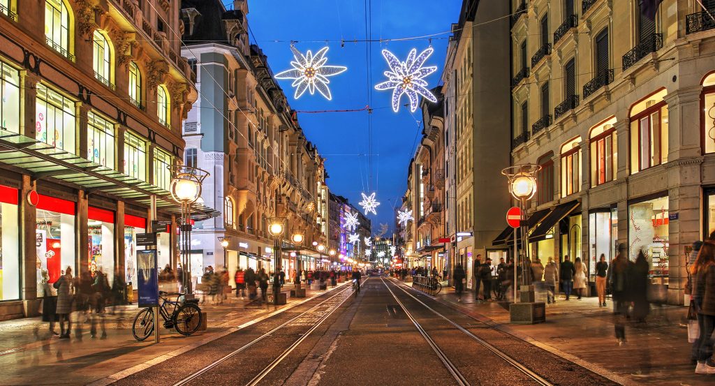 Rue animée de Genève en soirée, ornée de décorations lumineuses en forme d’étoiles pendant la période des fêtes.