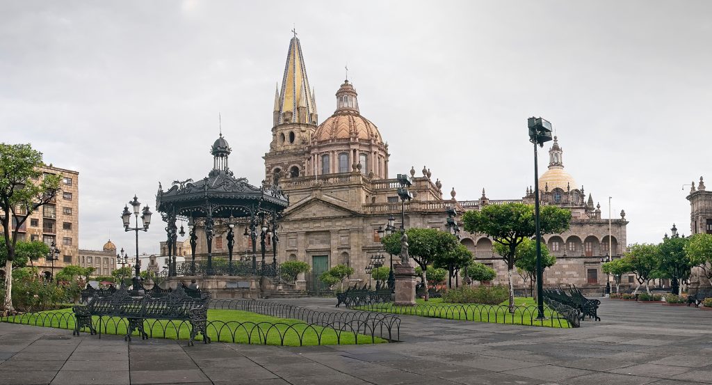 Historic city center of Guadalajara with the Guadalajara Cathedral and its iconic twin spires, surrounded by ornate lampposts and iron benches in a peaceful plaza.