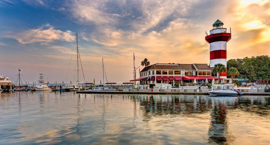 The iconic red-and-white striped Harbour Town Lighthouse at golden hour, reflecting off the marina waters of Hilton Head Island.