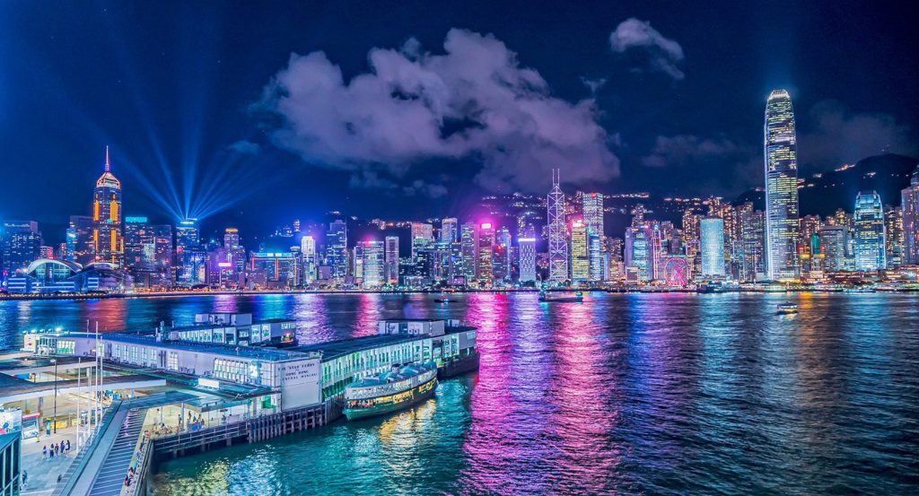Dazzling skyline of Hong Kong at night with the Symphony of Lights show illuminating Victoria Harbour, skyscrapers glowing in every color.