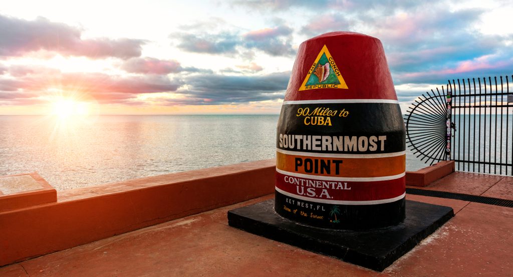 Vista del amanecer en la boya del punto más al sur en Key West, Florida, con el océano y el cielo brillando en tonos cálidos.