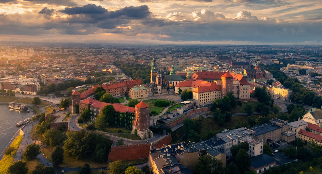 Aerial view of Kraków’s Wawel Castle at golden hour, perched above the Vistula River with the historic Old Town in the distance.