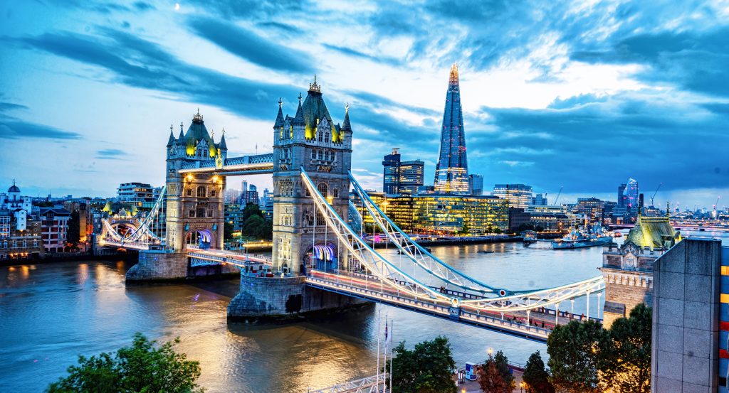 Iconic Tower Bridge lit up at dusk, with The Shard and modern buildings reflecting off the Thames.