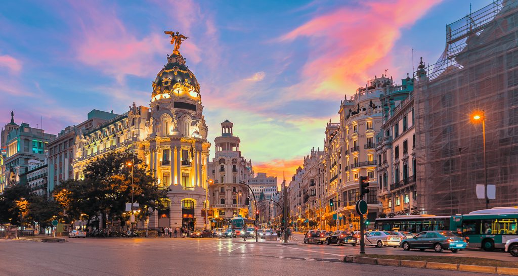 Gran Vía at golden hour with historic architecture, bustling traffic, and the iconic Metropolis Building glowing at sunset.