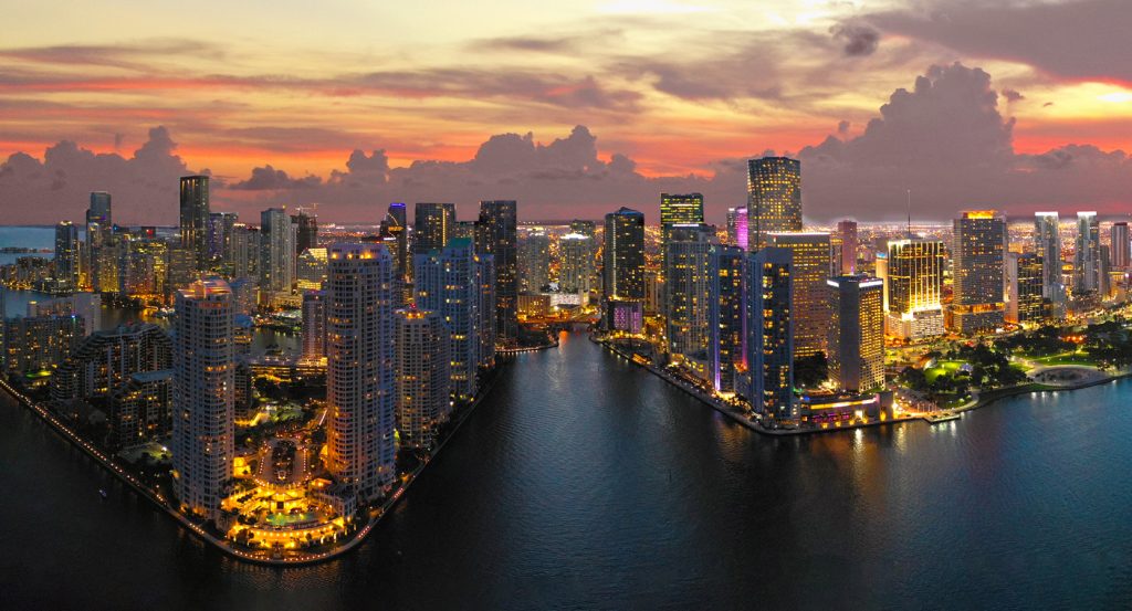 Aerial view of Downtown Miami lit up at sunset with Biscayne Bay in the foreground
