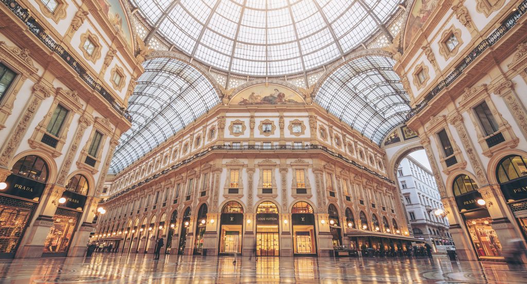 Elegant 19th-century shopping arcade in Milan featuring high-end boutiques beneath a grand vaulted glass roof.