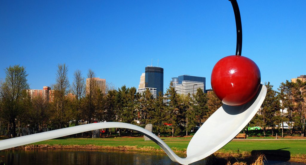A giant cherry atop a spoon sculpture over a pond at the Minneapolis Sculpture Garden on a clear day.