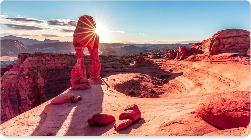 A hiker stands at the edge of a cliff in Moab, silhouetted against the vibrant orange and pink horizon.