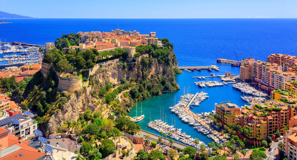 Luxury yachts docked at Port Hercules in Monte Carlo, surrounded by vibrant architecture and coastal cliffs.