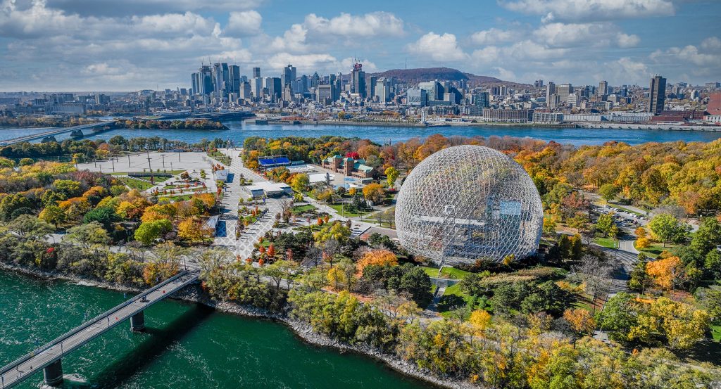 Geodesic dome of the Montreal Biosphere on Île Sainte-Hélène with fall foliage and downtown Montreal across the river.