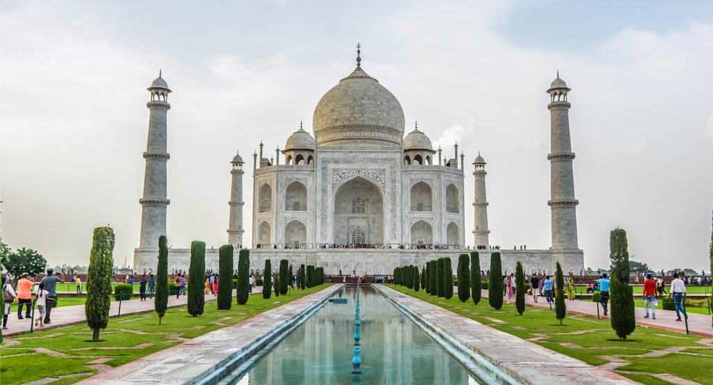Front view of the Taj Mahal framed by minarets and lush gardens, with crowds of visitors.