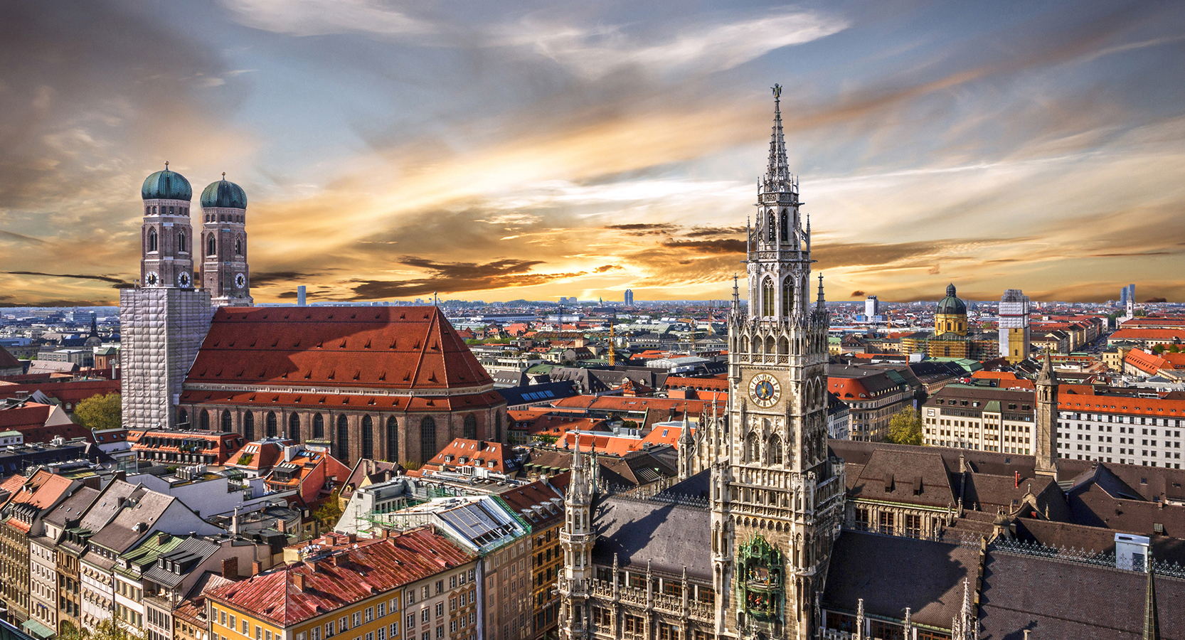 Sunset skyline over Munich’s Frauenkirche and Neues Rathaus, with historic rooftops and golden light dancing across the city.