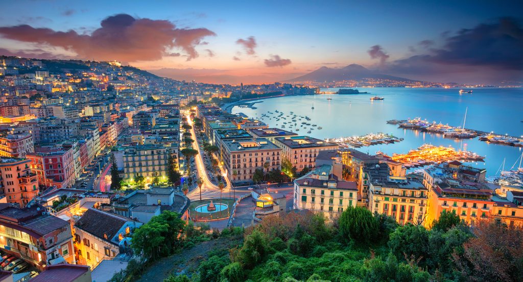 Evening lights illuminate Naples’ waterfront and hillside neighborhoods by the bay