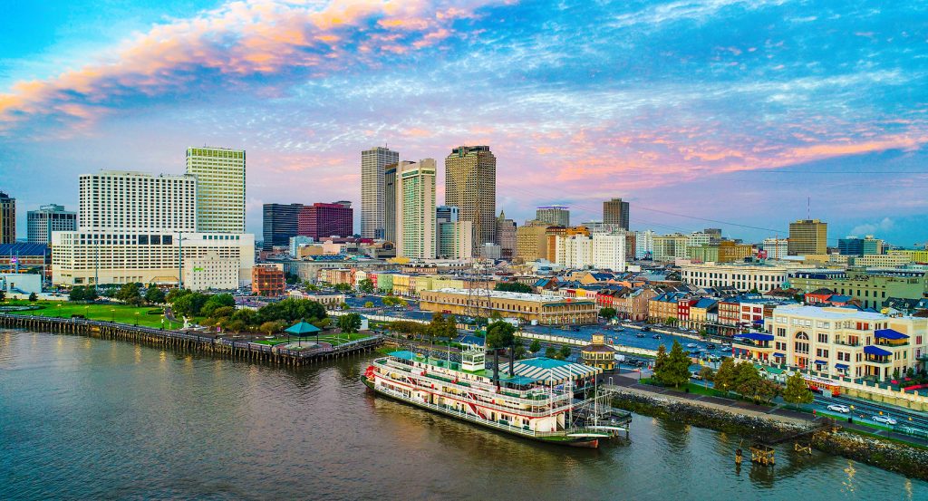 Colorful cityscape of New Orleans with historic architecture along the waterfront and a classic paddle steamer.