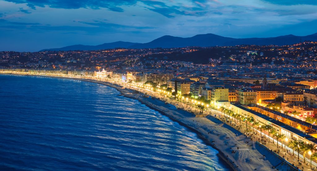 Twilight along the Promenade des Anglais glows with golden lights reflecting off the Mediterranean, with pastel buildings lining the lively shore.
