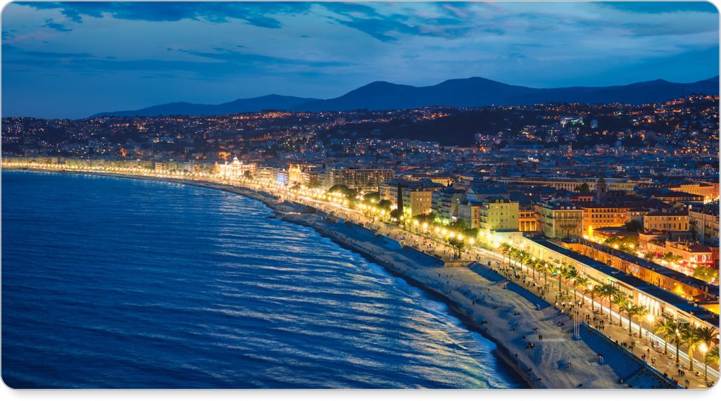 Locals and travelers alike lounging on the rocky beaches of Nice under striped umbrellas at sunset.