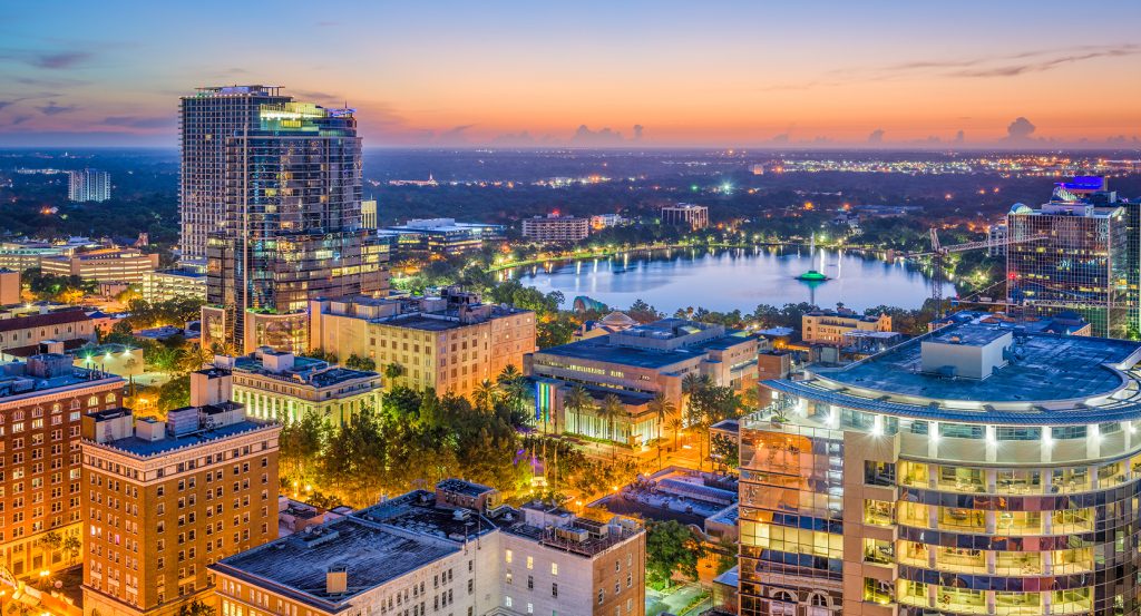 Vibrant cityscape of Orlando at twilight featuring high-rise buildings and Lake Eola’s glowing fountain.