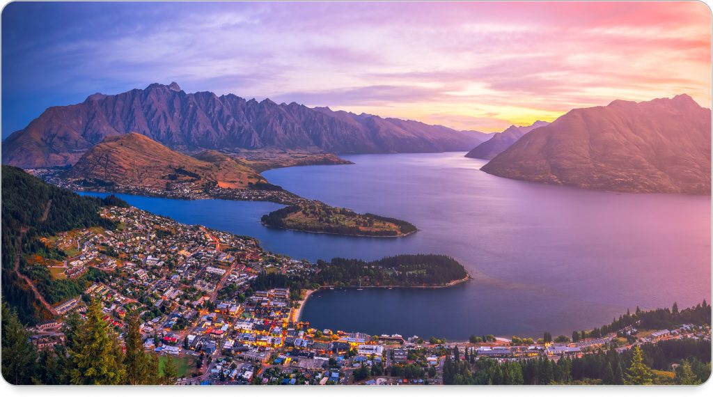 A serene twilight view of Queenstown’s lakefront with boats docked and the Remarkables in silhouette.