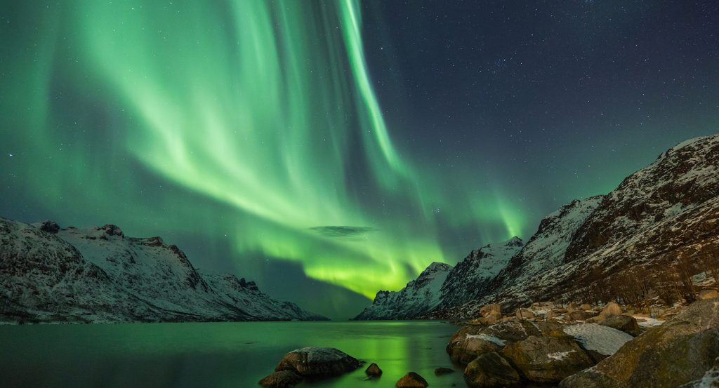 Aurora borealis dances across a star-studded sky above icy peaks and tranquil waters outside Reykjavík.