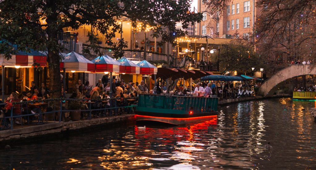 Lively restaurants and lit-up canal boats on San Antonio’s River Walk at dusk