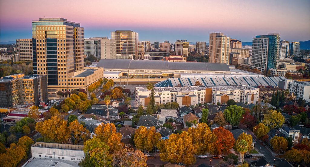 Downtown San Jose skyline at sunset with tech-centric high rises, leafy neighborhoods, and the iconic convention center in view.