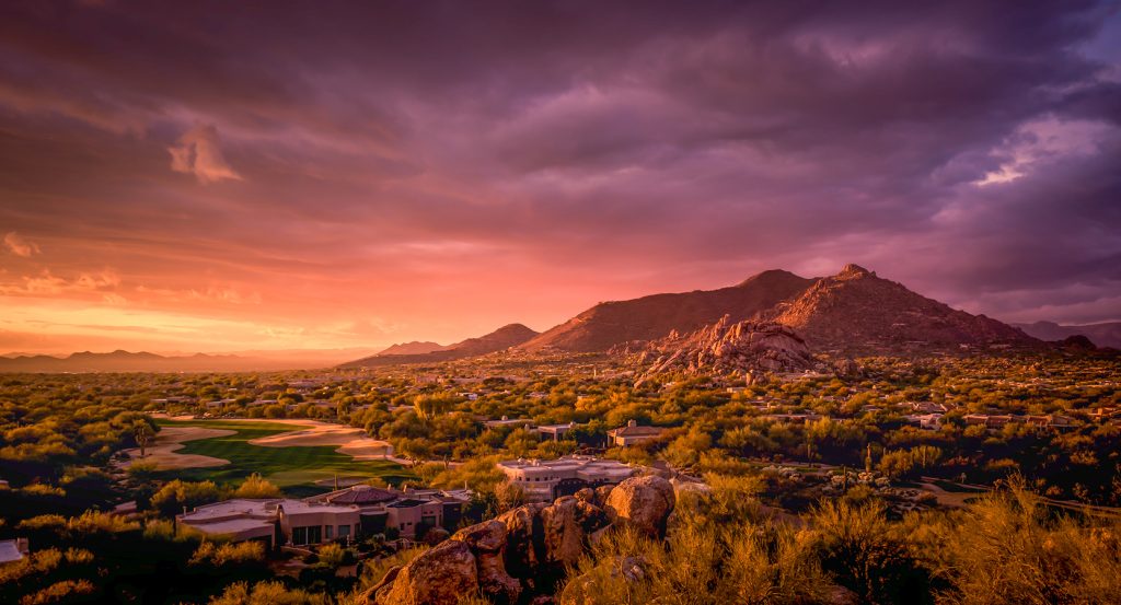 Golden hour over Scottsdale, Arizona, with rocky peaks and desert brush lit by glowing sunlight.