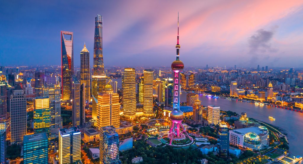 Evening skyline of Lujiazui with the Oriental Pearl Tower lit in vibrant colors, reflecting off the Huangpu River as boats cruise past.