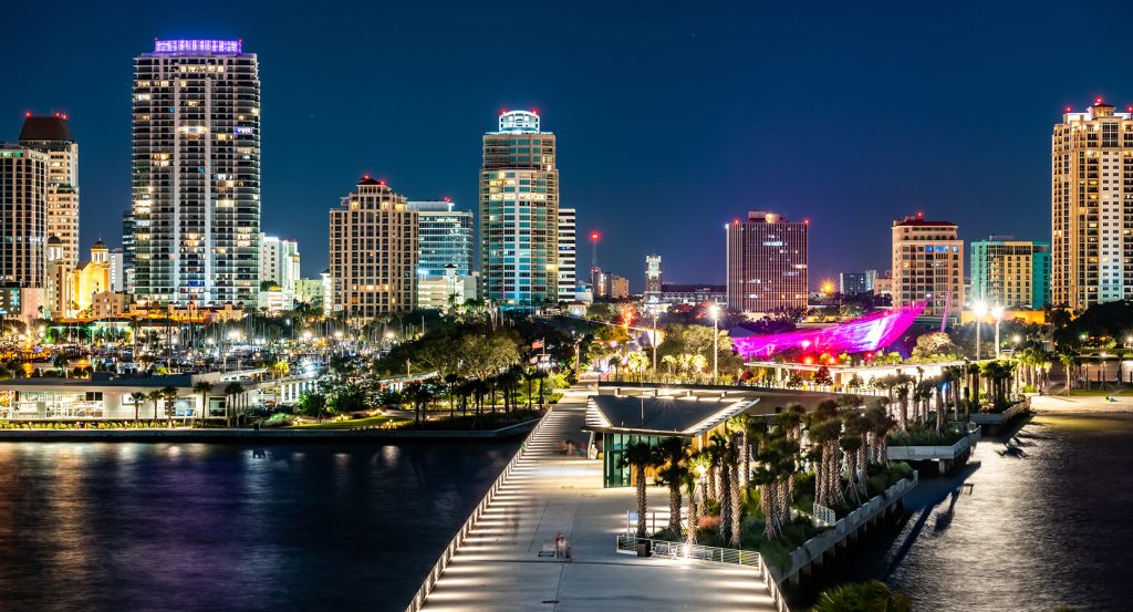 Vibrant night view of downtown Saint Petersburg, Florida, featuring illuminated waterfront architecture, high-rise buildings, and the striking pink-lit structure at the St. Pete Pier.