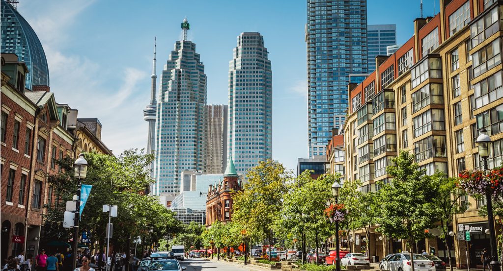 Cityscape view of Toronto’s Financial District with cars and pedestrians along a tree-lined street on a sunny day.