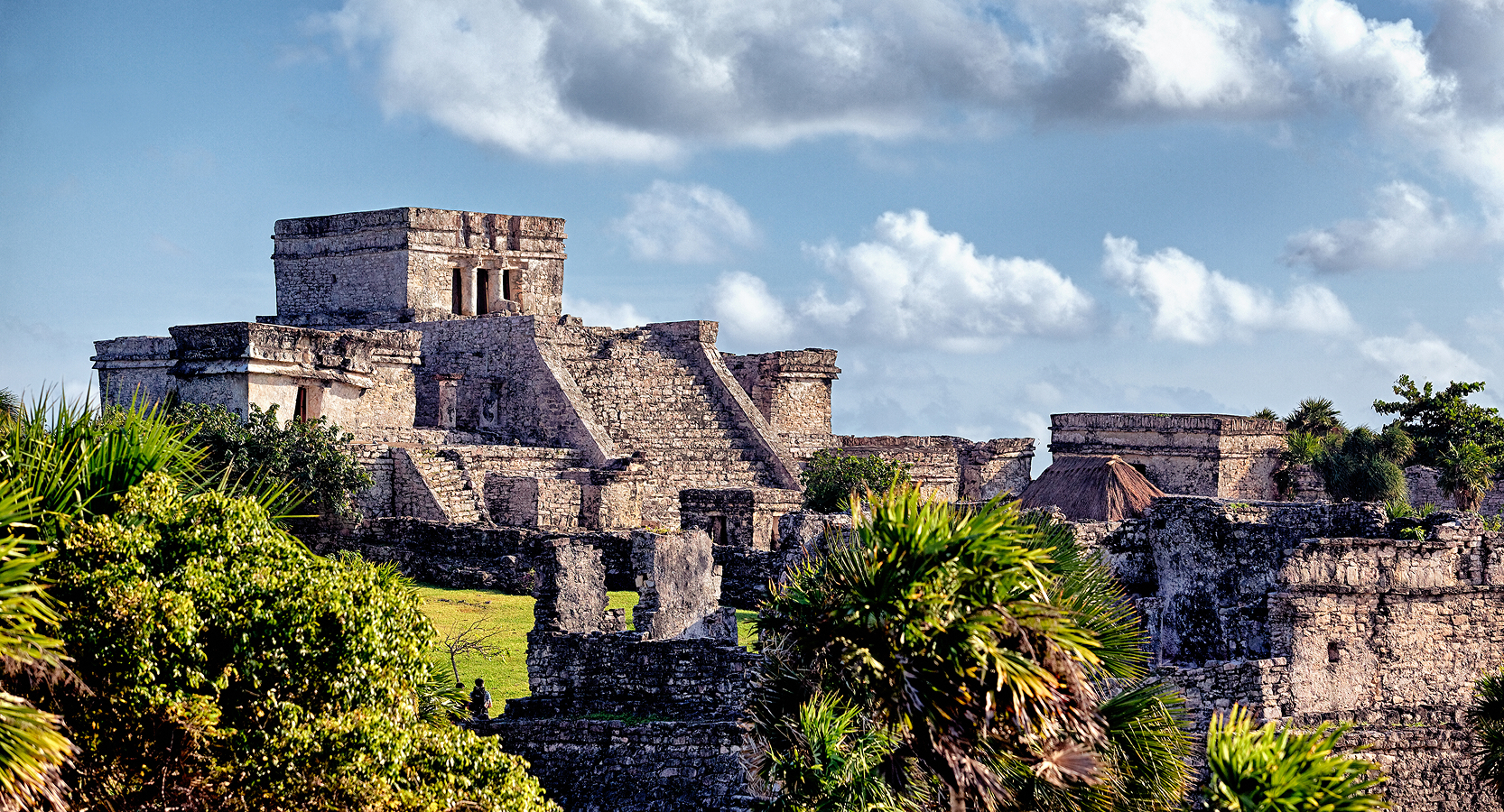 Stone temples of Tulum’s archaeological site surrounded by palm trees and historic remnants.