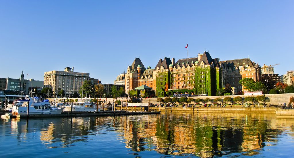 Waterfront view of The Fairmont Empress hotel in Victoria, British Columbia, with historic ivy-covered architecture and docked boats under clear skies.