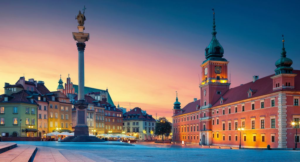 Sunset over Warsaw’s Old Town Square featuring the Royal Castle and Sigismund’s Column, with pastel townhouses and warm evening light.