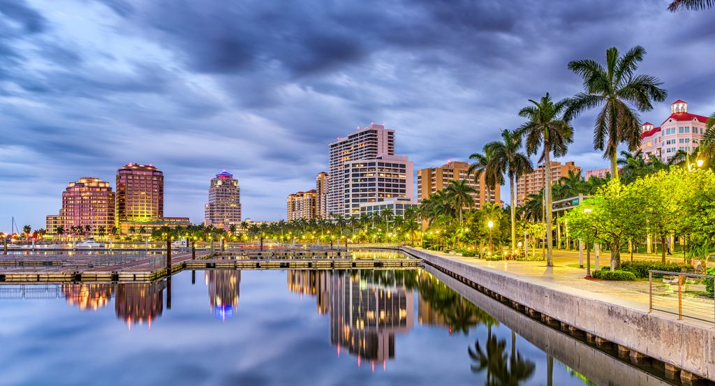 Cityscape of West Palm Beach, Florida with glowing lights and palm-lined promenade at dusk