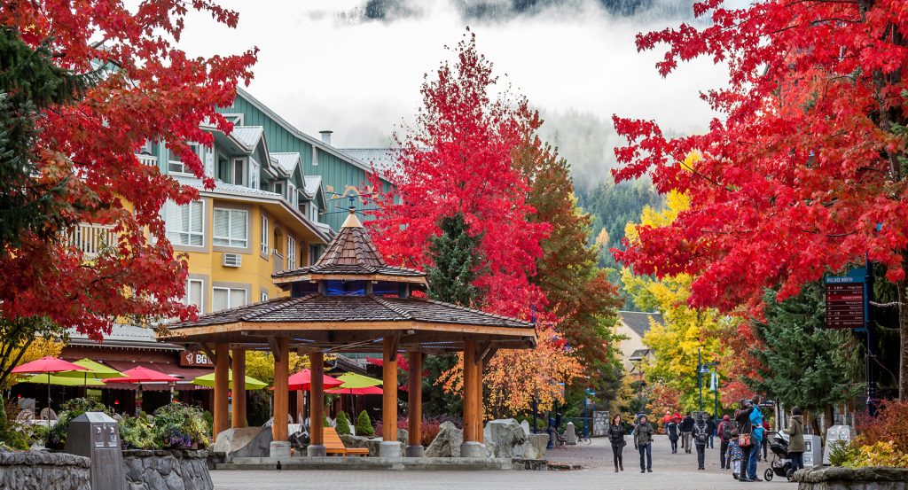 A cozy village scene in Whistler, British Columbia, framed by brilliant fall foliage and misty mountain peaks.