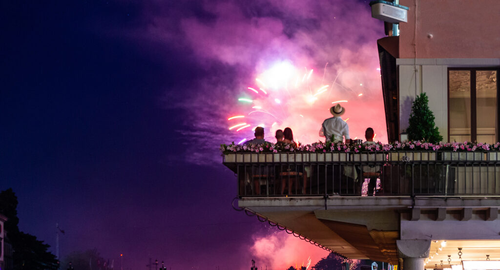 Balcony view of Zurich Festival with silhouettes against vibrant purple and red fireworks in the night sky