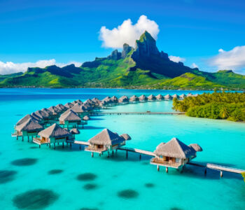 Thatched overwater bungalows stretch into turquoise waters with a lush mountain in the background in Bora Bora.