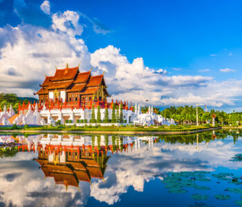 Traditional Lanna-style temple reflected in a calm water garden in Chiang Mai under a vibrant blue sky.