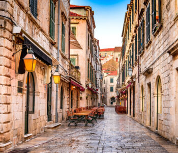 Stone alleyway with shuttered windows and empty café tables in Dubrovnik