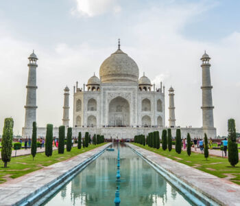 Iconic white marble Taj Mahal with reflection pool and tourists in Agra, India.