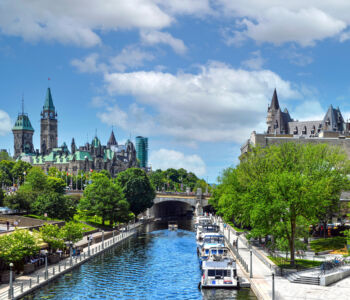 A scenic view of Ottawa’s Parliament buildings and the Fairmont Château Laurier overlooking the Rideau Canal on a sunny day.